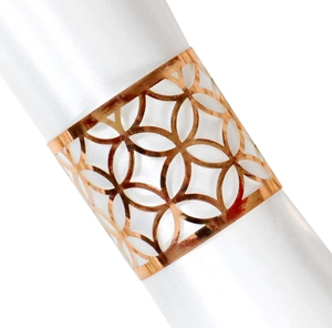 Detalle del servilletero de metal oro rosa con diseño floral geométrico sobre satén blanco