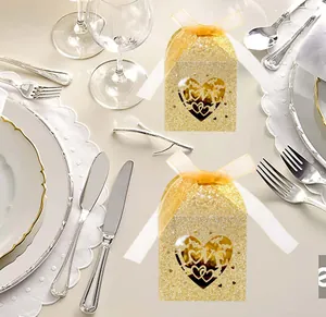 Detail of gold glitter laser cut LOVE candy boxes with ribbon on elegant dinner plate