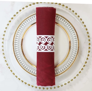 Detail of white laser-cut paper napkin ring with burgundy fabric on gold-rimmed plates