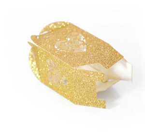 Macro shot of laser-cut heart detail on golden glitter wedding favor candy box
