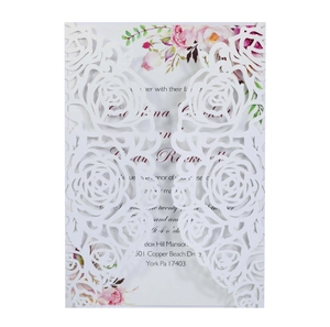 Macro shot of white laser-cut wedding invitation featuring intricate rose patterns