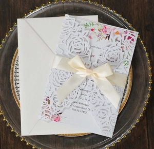 Macro detail of laser-cut rose hollow invitation with cream ribbon and floral inner card