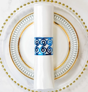 Close-up of a glossy blue hollow metal napkin ring on a white fabric napkin at a table