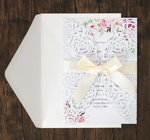 Detailed laser-cut rose invitation card set with elegant ribbon on dark wood background