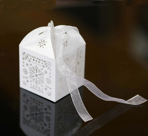 White laser-cut snowflake wedding candy box with ribbon on reflective black background