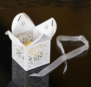 Detail of laser-cut snowflake gift box in ice white with ribbon and golden candy