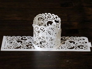 Detailed laser-cut paper candle holder with elegant white floral patterns on wood background
