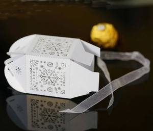 Laser cut white snowflake gift box with ribbon on a glossy reflective surface