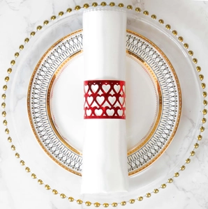 Detail of red hollow heart napkin ring with laser-cut design on white marble surface
