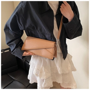 Detail of camel leather crossbody bag styled with black jacket and white skirt