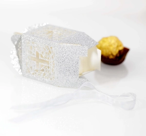 Macro detail of laser-cut cross on silver glitter gift box with white ribbon tie
