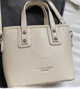 Detail of beige lychee grain leather tote bag with sturdy handles and metallic rivets