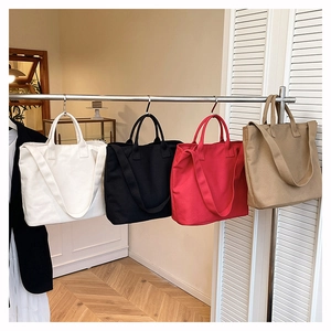 Detailed display of large canvas tote bags in white, black, red, and khaki on a rack