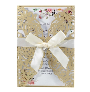 Macro detail of laser-cut rose patterns on gold card with satin ribbon and invitation insert