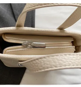 Detailed close-up of smooth metal zipper and lychee pattern leather texture on beige bag