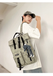 Side view of a large grey-green wash style backpack with decorative plush doll pendant