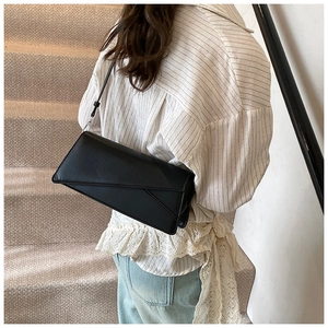 Minimalist black faux leather crossbody bag featuring an asymmetric folding flap detail