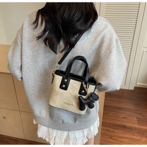 Détail du sac seau en toile avec bordure en cuir noir et breloque chiot sur la bandoulière