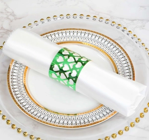 Detail of green hollow heart napkin ring on a white napkin over a golden-rimmed plate