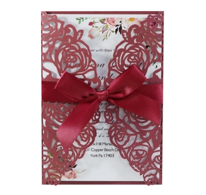 Detail of burgundy laser-cut floral wedding invitation with silk ribbon bow and insert