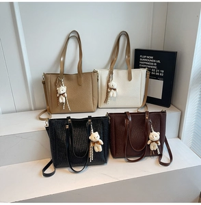 Close-up of four woven tote bags in various colors featuring leather straps and bear charms