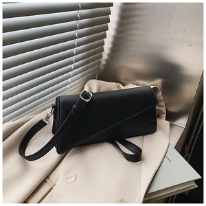 Close-up of black crossbody square bag with asymmetric flap on a beige blazer jacket