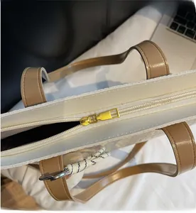 Close-up of golden smooth zipper on cream woven tote bag with camel leather trim