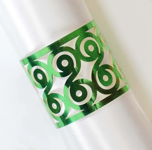 Detail of laser-cut green metallic napkin ring with intricate scrolls on white satin