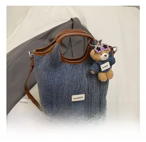 Detail of blue denim bucket bag with brown leather handles and cute teddy bear charm