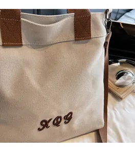 Detail view of durable canvas tote with brown straps and metallic shoulder strap clips