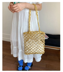 Detail of gold metallic woven tote bag featuring rope handles and white drawstring liner