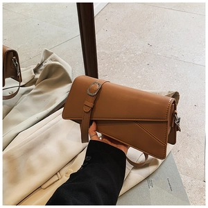 Detail of caramel brown asymmetrical shoulder bag with silver buckle and matte leather