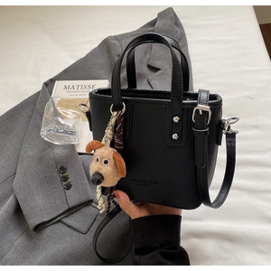 Detail of black pebbled leather bucket bag with dog pendant and adjustable shoulder strap
