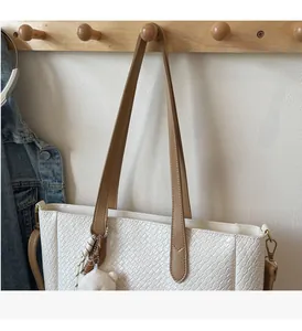 Detail of white woven tote bag with brown leather strap and plush bear charm decoration