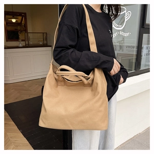 Close-up of a large khaki canvas tote bag featuring dual handles and a wide shoulder strap