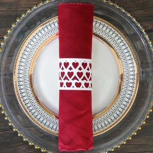 Close-up of laser-cut white heart pattern paper napkin ring on a red cloth napkin