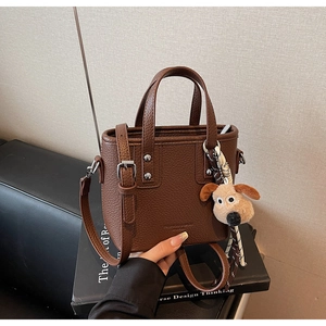 Detail of brown litchi pattern leather bucket bag with cute plush puppy keychain
