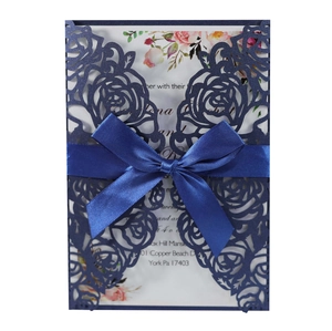 Close-up of navy blue laser-cut rose wedding invitation with a satin ribbon and floral insert