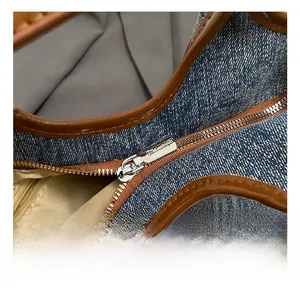 Detail of metal zipper and brown leather trim on denim bucket bag with fabric lining