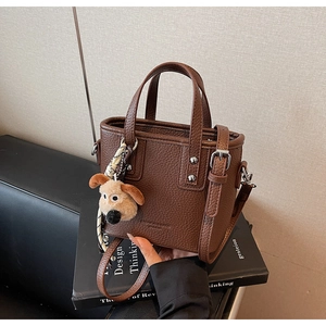 Detail of dark brown pebble leather tote bag with silver studs and plush dog charm