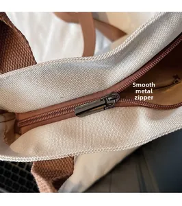 Detail of smooth black metal zipper on off-white canvas tote with brown trim