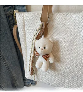 Detail of white plush bear charm with brown Love bow on a woven tote bag strap