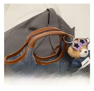 Detailed shot of dark blue denim bag with brown leather handles and teddy bear charm