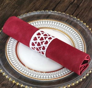 Detail of white laser-cut hollow heart napkin ring on a burgundy cloth for wedding decor