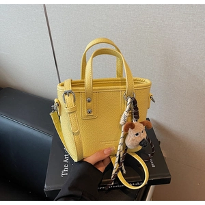 Close-up of bright yellow litchi grain bucket bag with cute plush puppy keychain