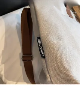 Close-up of cream canvas tote bag showing black woven label and dark brown strap detail