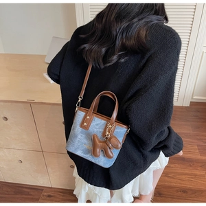 Détail du sac seau en denim bleu avec garniture en cuir marron et breloque chien 3D