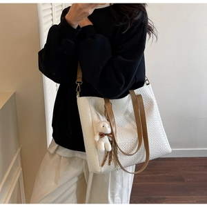 Detail of white woven leather tote bag with brown straps and cute plush bear charm