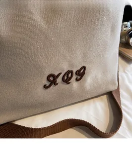 Close-up of cream canvas tote bag featuring embroidered XOG lettering and brown strap