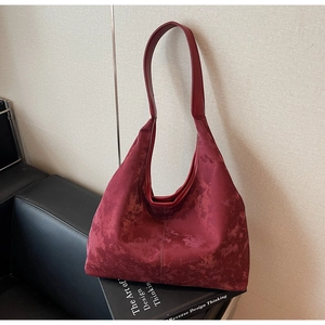 Artistic close-up of a burgundy suede half-moon tote bag placed on a design book